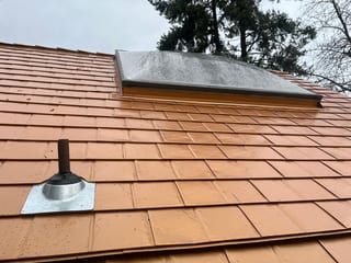 Close-up of Interlock Copper Penny aluminum slate roofing with a vent pipe boot flashing and framed skylight on a steep Portland home roof.