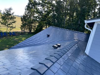 Aerial view of a deep charcoal Interlock aluminum slate metal roof with complex hip valleys on a rural Craftsman home surrounded by vineyard and trees.