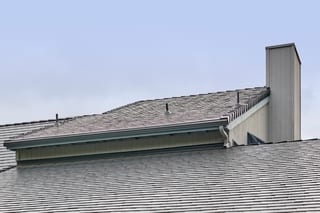 Deep charcoal Interlock aluminum slate metal roofing on a multi-level home in Amity, OR, featuring a tall chimney, vent pipes, and ridge caps.