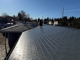 Deep charcoal Interlock aluminum slate metal roofing on a single-family ranch home in Beaverton, OR, showing full roof with chimney and valley details.