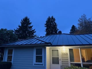 Single-story ranch home in Portland OR with a hunter green Interlock standing seam aluminum hip roof photographed at twilight.