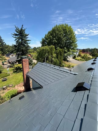 Aerial view of a complex Craftsman home roof clad in Interlock deep charcoal aluminum slate tiles with a red brick chimney and multiple skylights in Gresham, OR.