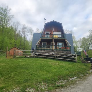 Three-story A-frame cabin in Vermont with hunter green Interlock aluminum shingle roof, multi-tiered decks, and wood siding set against a forested hillside.