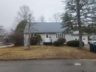 Front elevation of a single-family Ranch home with an Interlock deep charcoal aluminum slate metal roof, attached garage, and brick chimney, South Burlington, VT.