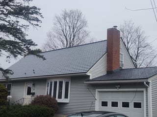 Cape Cod home in South Burlington VT with Interlock deep charcoal aluminum slate metal roof, prominent brick chimney, and gray vinyl siding.
