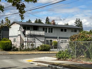 Charcoal Grey Interlock Tile aluminum roof on a two-storey grey home with a metal roof among tall trees, Seattle, Washington