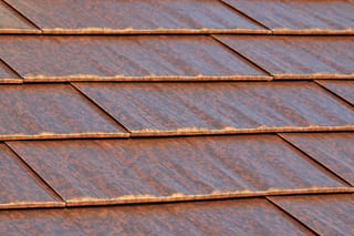 Aged Copper Interlock Cedar Shingle aluminum roof on a brown two-storey home with dormers among tall pines, Burien, Washington