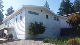 Before: the old roof on a white ranch-style home with a metal roof among trees, Des Moines, Washington, ahead of a Black Interlock Standing Seam aluminum roof