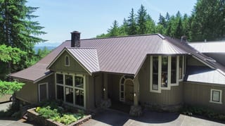 Tudor Brown Interlock Standing Seam aluminum roof on a brown two-storey home with dormers among tall pines, Fall City, Washington