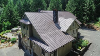 Tudor Brown Interlock Standing Seam aluminum roof on a brown two-storey home with dormers among tall pines, Fall City, Washington