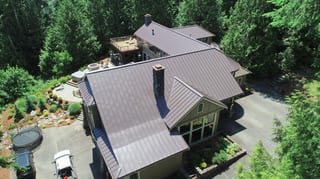 Tudor Brown Interlock Standing Seam aluminum roof on a two-storey home with a brown metal roof among tall trees, Fall City, Washington