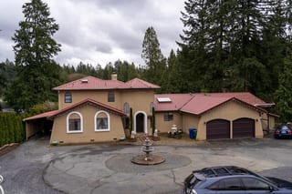 Tile Red Interlock Tile aluminum roof on a tan two-storey home with a red metal roof in a wooded area, Woodinville, Washington