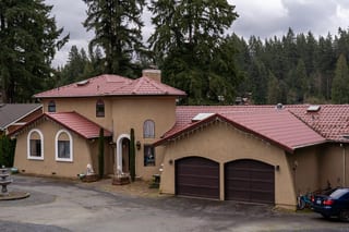 Tile Red Interlock Tile aluminum roof on a tan stucco home with a red metal roof among tall, Woodinville, Washington