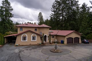 Tile Red Interlock Tile aluminum roof on a tan single-storey Mediterranean home among tall evergreens, Woodinville, Washington