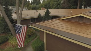 Aged Copper Interlock Cedar Shingle aluminum roof on a brown single-storey home with a gable roof among tall, Bellevue, Washington