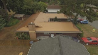 Aged Copper Interlock Cedar Shingle aluminum roof on a brown ranch-style home with a metal roof among tall trees, Bellevue, Washington