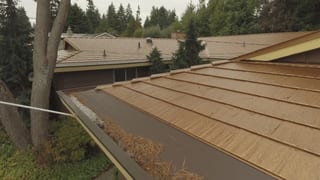 Aged Copper Interlock Cedar Shingle aluminum roof on a brown single-family home with dormers among tall pines, Bellevue, Washington