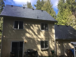 Black Interlock Slate aluminum roof on a two-storey home with a black metal roof among tall trees, Poulsbo, Washington