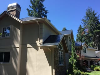 Black Interlock Slate aluminum roof on a beige modern home with a metal roof among tall trees, Bothell, Washington