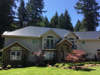 Black Interlock Slate aluminum roof on a beige two-storey home with dormers among tall pines, Bothell, Washington