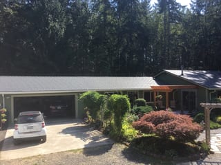 Deep Charcoal Interlock Slate aluminum roof on a green single-storey home with a metal roof among tall, Poulsbo, Washington