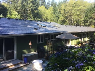 Deep Charcoal Interlock Slate aluminum roof on a two-storey green home with a metal roof in a forested area, Poulsbo, Washington