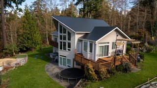 Black Interlock Slate aluminum roof on a white house with a black metal roof in a forested area, Langley, Washington