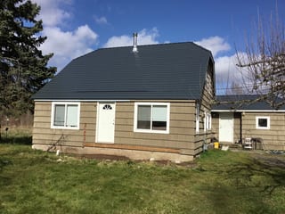 Deep Charcoal Interlock Slate aluminum roof on a tan single-family home with a metal roof in a forested, Tacoma, Washington
