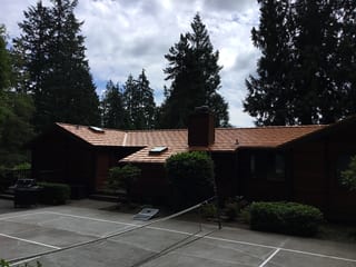 Copper Penny Interlock Shake aluminum roof on a dark red ranch-style home with chimney among tall, Bainbridge Island, Washington