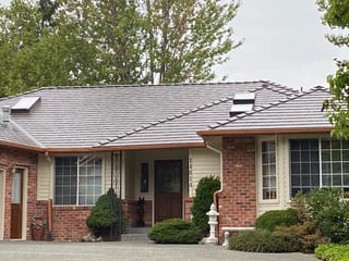 Tudor Brown Interlock Cedar Shingle aluminum roof on a Tudor home with brick and cream siding among forested, Mill Creek, Washington
