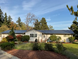 Deep Charcoal Interlock Slate aluminum roof on a white ranch style home with a metal roof among tall trees, Tacoma, Washington