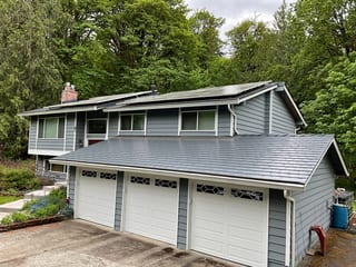 Deep Charcoal Interlock Slate aluminum roof on a grey two-storey home with dormers among tall pines, Woodinville, Washington
