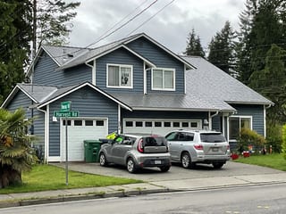 Musket Grey Interlock Slate aluminum roof on a grey two-storey craftsman home with a garage among tall, Bothell, Washington