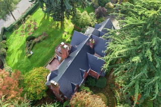 Black Interlock Slate aluminum roof on a red brick home with a slate roof among tall trees in the, Seattle, Washington