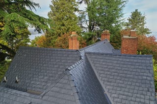 Black Interlock Slate aluminum roof on a dark grey two-storey home with dormers among tall conifers, Seattle, Washington