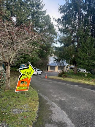 Street-view of a single-family home in Lakewood WA with a newly installed black Interlock aluminum cedar shingle metal roof, framed by tall evergreens.