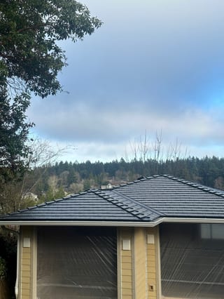 Black Interlock aluminum cedar shingle metal roof on a single-family craftsman home with multi-hip complexity, set against a forested suburban backdrop in Lakewood, WA.
