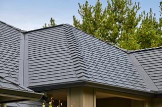 Close-up of a complex multi-hip Interlock aluminum slate roof in charcoal black on a single-family Craftsman home surrounded by pine trees in Ridgefield, WA.