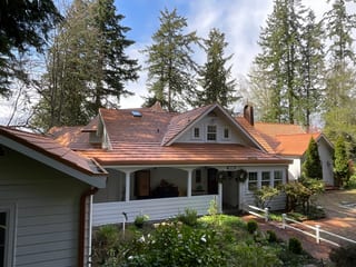 Copper Penny Interlock Shake aluminum roof on a cream two-storey Craftsman home with dormers among tall, Bremerton, Washington
