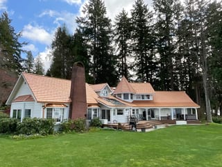 Copper Penny Interlock Shake aluminum roof on a white one-storey craftsman style home among tall, Bremerton, Washington