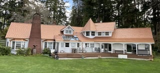 Copper Penny Interlock Shake aluminum roof on a white two-storey Colonial home with dormers among tall, Bremerton, Washington