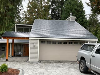 Deep charcoal Interlock aluminum slate metal roof on a Craftsman-style home in Bellevue, WA, featuring a hip roof, chimney, and covered front entry.