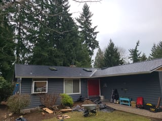 Front elevation of a gray ranch home with a newly installed Interlock black aluminum slate metal roof, skylights, and red front door in Redmond, WA.