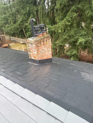 Black Interlock Slate aluminum roof on a black single-storey home with a gable roof among tall, Redmond, Washington