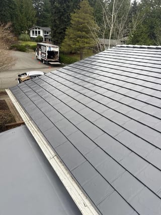 Black Interlock Slate aluminum roof on a grey two-storey home with dormers among tall pines, Redmond, Washington