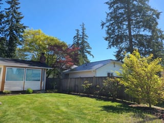 Deep Charcoal Interlock Slate aluminum roof on a two-storey home with a metal roof among tall trees, Lynnwood, Washington