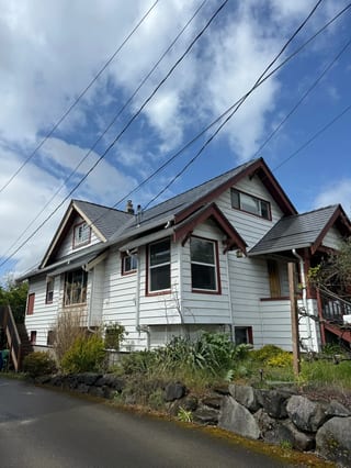 Musket Grey Interlock Slate aluminum roof on a white two-storey Craftsman home among tall trees, Seattle, Washington