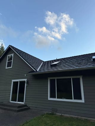 Black Interlock Shake aluminum roof on a dark grey home with a gable and dormers among tall trees, Marysville, Washington