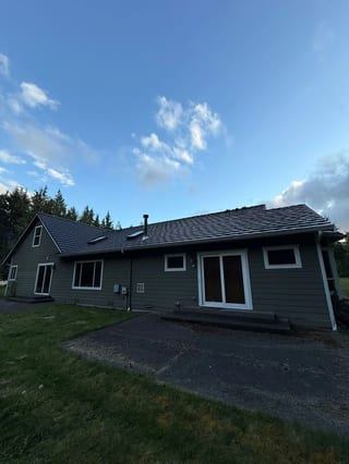 Black Interlock Shake aluminum roof on a green single-storey home with a metal roof among tall, Marysville, Washington