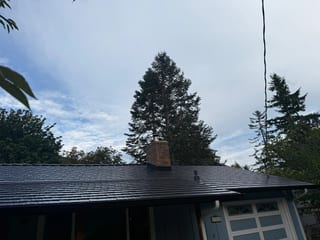 Black Interlock Cedar Shingle aluminum roof on a blue single-family home with dormers among tall pines, North Bend, Washington